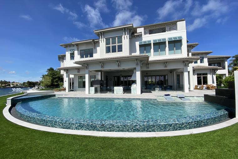Custom gunite pool with a curved sun shelf beside a modern two-storey South Florida home