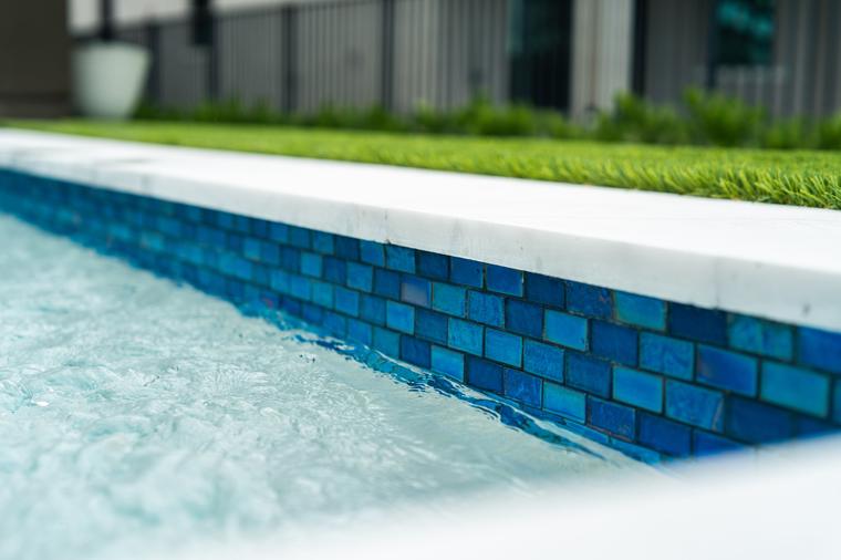 Close-up of blue glass waterline tile and white coping at the edge of a pool