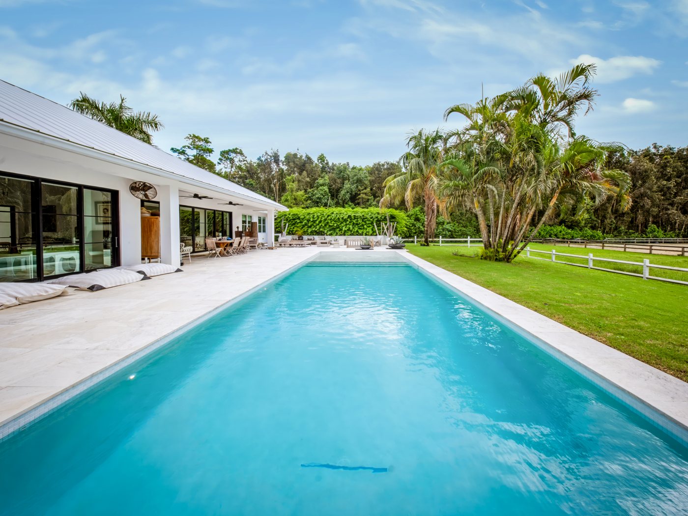 PebbleSheen Arctic White pool finish on a long lap pool beside a white South Florida home with a travertine deck