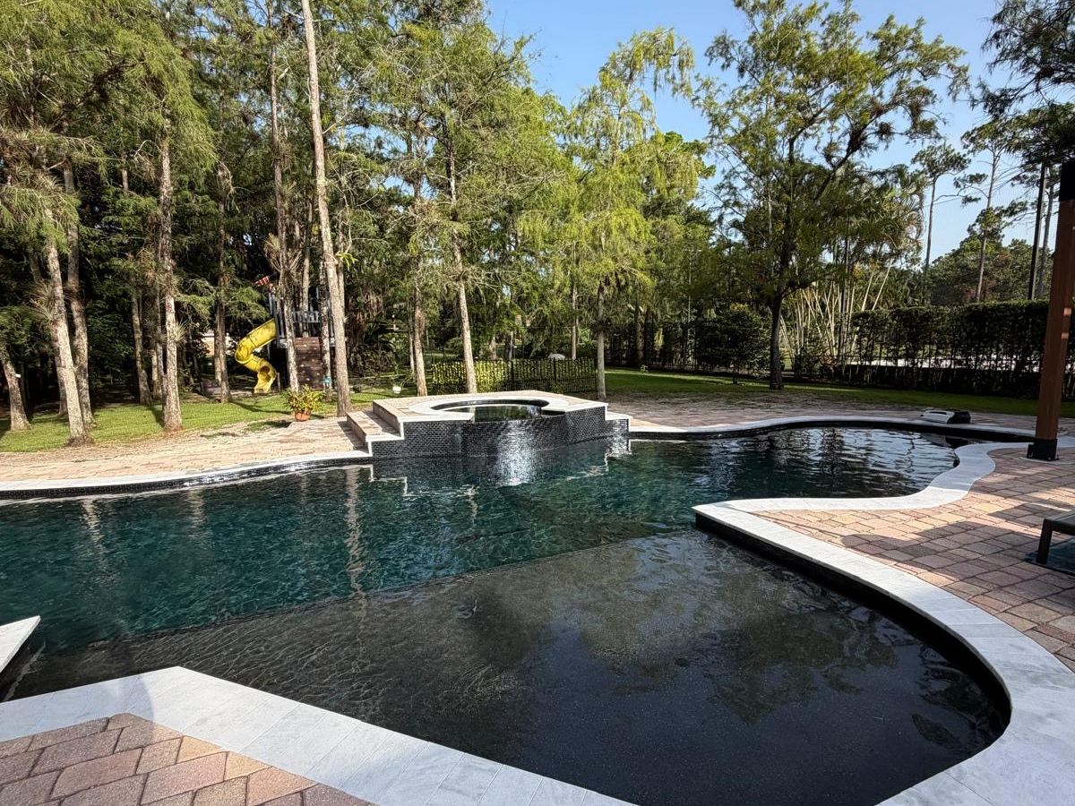 PebbleSheen Black Eclipse pool finish on a freeform pool and spa with a paver deck in South Florida