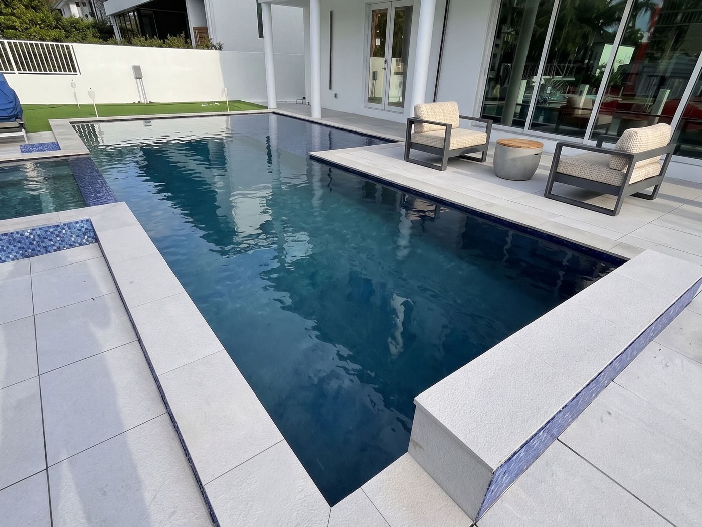PebbleSheen Blue Surf pool finish on a rectangular pool with a spa and light stone deck beside a modern South Florida home